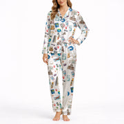 Woman wearing a white long-sleeve pajama set with a colorful watercolor travel-themed print featuring landmarks like the Statue of Liberty, Eiffel Tower, and hot air balloons, standing in a bedroom.