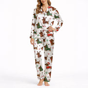A woman wearing a white short sleeve pajama set with shorts, featuring a festive Christmas pattern of cartoon dachshunds dressed as Santa, reindeer, and Christmas trees. The pajamas have red piping.