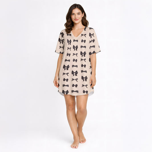 A women's short sleeve button-down pajama set with shorts, featuring a repeating pattern of small black bow ties on a light beige background. The set has black piping details and is made from a soft knit fabric.
