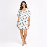Women's pajama set with short sleeves and shorts, featuring a repeating pattern of mallard ducks swimming in water with green grass, trimmed with green piping. The fabric is a soft, light-colored knit.