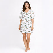 Women's pajama set with short sleeves and shorts, featuring a repeating pattern of mallard ducks swimming in water with green grass, trimmed with green piping. The fabric is a soft, light-colored knit.