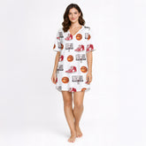 Woman wearing a white short sleeve button-down pajama set with red piping, featuring a fun basketball, sneaker, and hoop pattern.