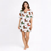 A woman wearing a white short sleeve pajama set with shorts, featuring a festive Christmas pattern of cartoon dachshunds dressed as Santa, reindeer, and Christmas trees. The pajamas have red piping.