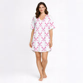 Women's white pajama set with pink crossed lacrosse sticks and balls pattern, featuring a button-down top and shorts, worn by a woman.