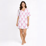 Women's white pajama set with pink crossed lacrosse sticks and balls pattern, featuring a button-down top and shorts, worn by a woman.