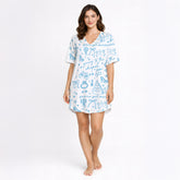 Woman wearing a white and light blue wedding-themed pajama set with short sleeves and shorts, holding a white mug. The pajama set features doodles of wedding cakes, rings, doves, and text 'going to the chapel' and 'gonna get married'.