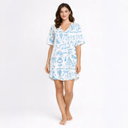 Woman wearing a white and light blue wedding-themed pajama set with short sleeves and shorts, holding a white mug. The pajama set features doodles of wedding cakes, rings, doves, and text 'going to the chapel' and 'gonna get married'.