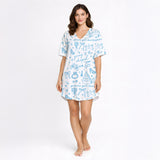 Woman wearing a white and light blue wedding-themed pajama set with short sleeves and shorts, holding a white mug. The pajama set features doodles of wedding cakes, rings, doves, and text 'going to the chapel' and 'gonna get married'.