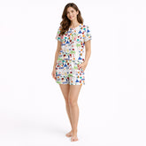 Women's pajama set featuring a vibrant Puerto Rico themed print with the flag, coqui frogs, palm trees, hibiscus flowers, and El Morro, on a white background.