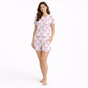 Women's white pajama set with pink crossed lacrosse sticks and balls pattern, featuring a button-down top and shorts, worn by a woman.
