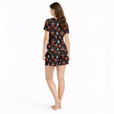 Women's Christmas pajama set featuring a festive pattern of cute Highland cows wearing Santa hats and plaid scarves, with white Christmas trees and snowflakes on a black background. The set includes a short-sleeve button-down top and matching shorts.
