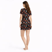 Women's Christmas pajama set featuring a festive pattern of cute Highland cows wearing Santa hats and plaid scarves, with white Christmas trees and snowflakes on a black background. The set includes a short-sleeve button-down top and matching shorts.
