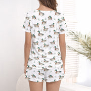 Women's pajama set with short sleeves and shorts, featuring a repeating pattern of mallard ducks swimming in water with green grass, trimmed with green piping. The fabric is a soft, light-colored knit.
