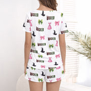 Women's pajama set featuring a 'Wicked' themed pattern with witch hats, pink bows, green bows, and pink dresses on a light background, made from soft knit fabric.