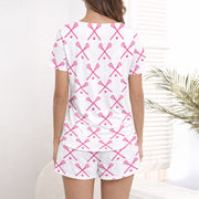 Women's white pajama set with pink crossed lacrosse sticks and balls pattern, featuring a button-down top and shorts, worn by a woman.