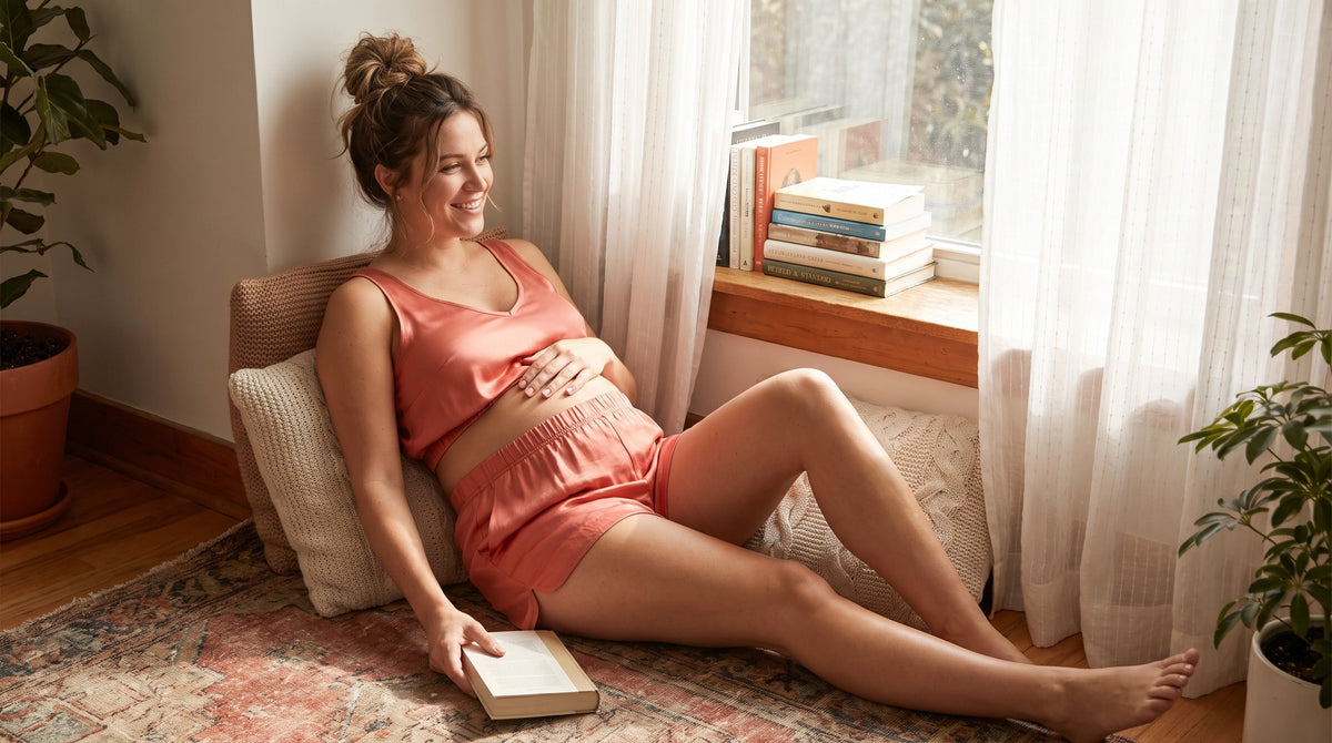 Pregnant woman wearing comfortable maternity two piece set lounging by sunny bedroom window