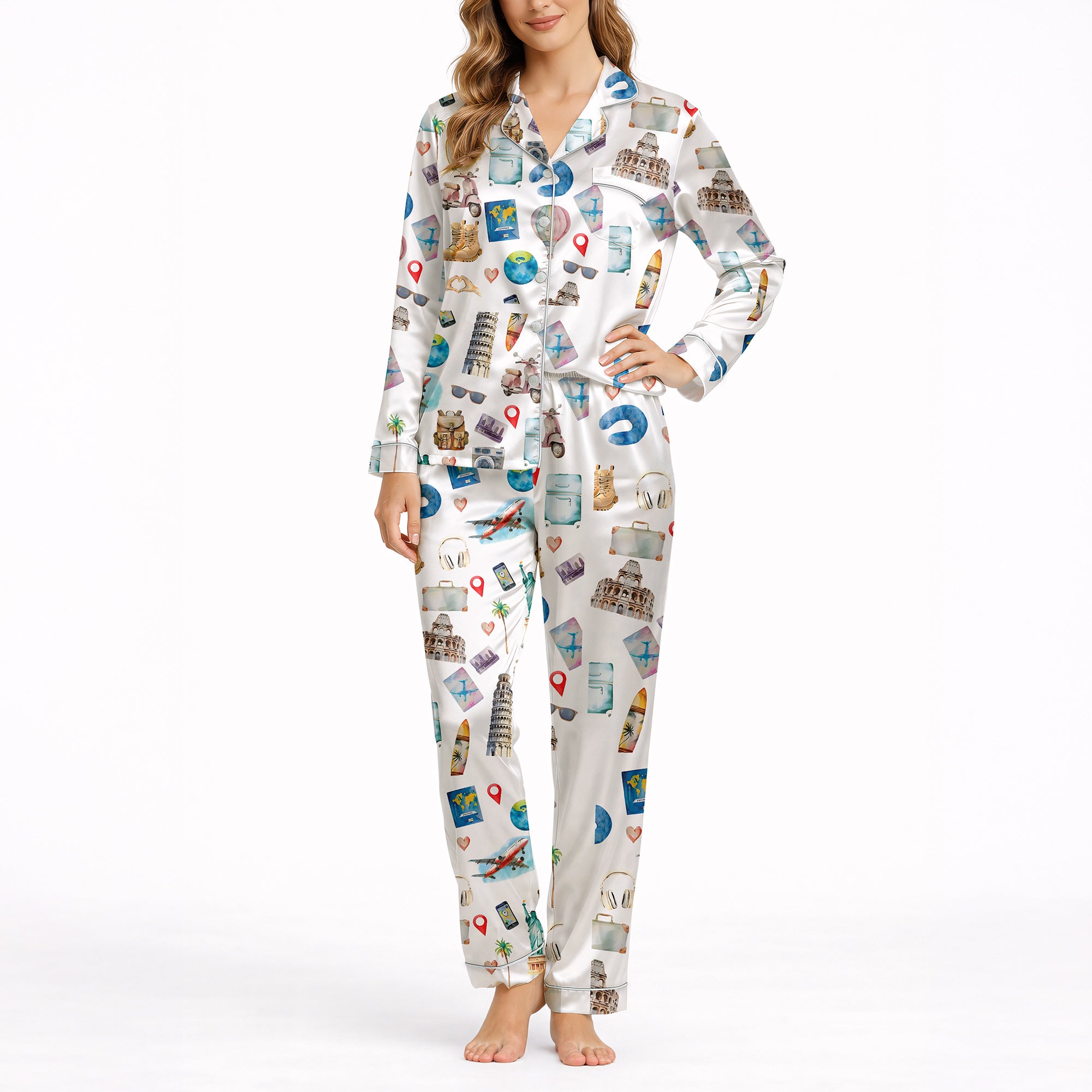 Woman wearing a white long-sleeve pajama set with a colorful watercolor travel-themed print featuring landmarks like the Statue of Liberty, Eiffel Tower, and hot air balloons, standing in a bedroom.