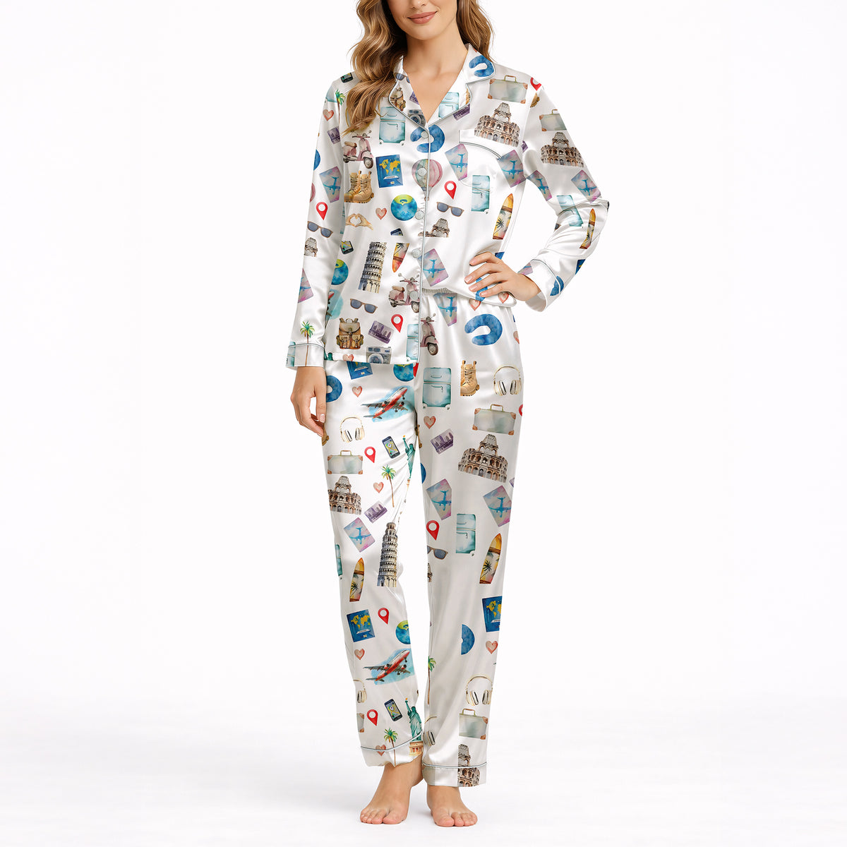 Woman wearing a white long-sleeve pajama set with a colorful watercolor travel-themed print featuring landmarks like the Statue of Liberty, Eiffel Tower, and hot air balloons, standing in a bedroom.