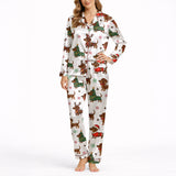 A woman wearing a white short sleeve pajama set with shorts, featuring a festive Christmas pattern of cartoon dachshunds dressed as Santa, reindeer, and Christmas trees. The pajamas have red piping.