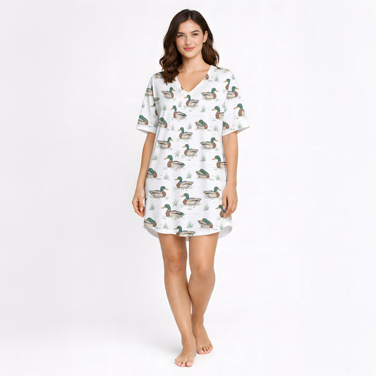 Women's pajama set with short sleeves and shorts, featuring a repeating pattern of mallard ducks swimming in water with green grass, trimmed with green piping. The fabric is a soft, light-colored knit.