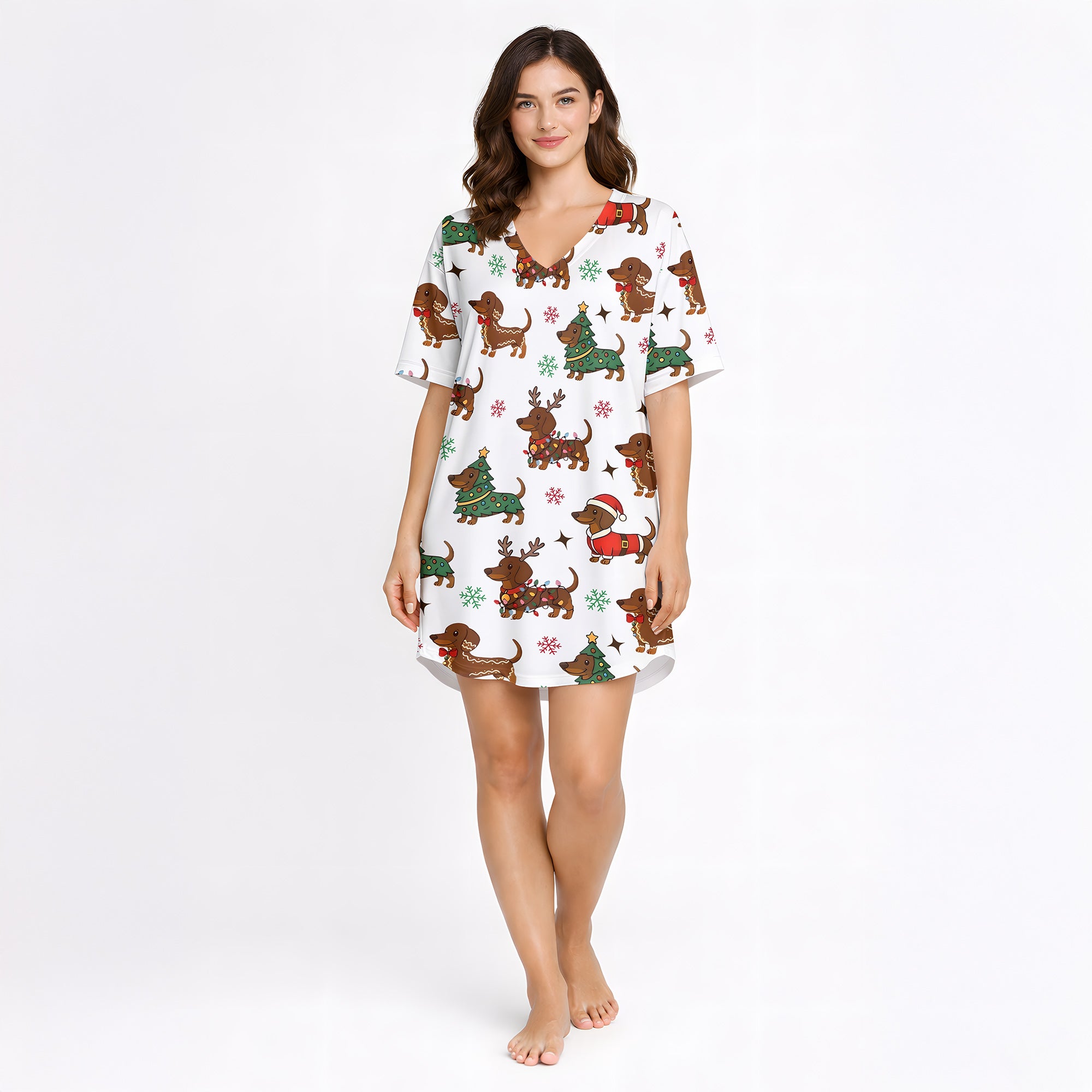 A woman wearing a white short sleeve pajama set with shorts, featuring a festive Christmas pattern of cartoon dachshunds dressed as Santa, reindeer, and Christmas trees. The pajamas have red piping.
