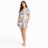 Women's pajama set featuring a vibrant Puerto Rico themed print with the flag, coqui frogs, palm trees, hibiscus flowers, and El Morro, on a white background.