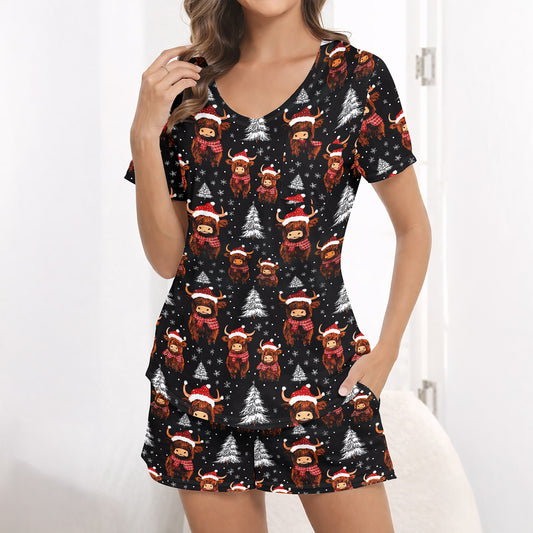 Women's Christmas pajama set featuring a festive pattern of cute Highland cows wearing Santa hats and plaid scarves, with white Christmas trees and snowflakes on a black background. The set includes a short-sleeve button-down top and matching shorts.